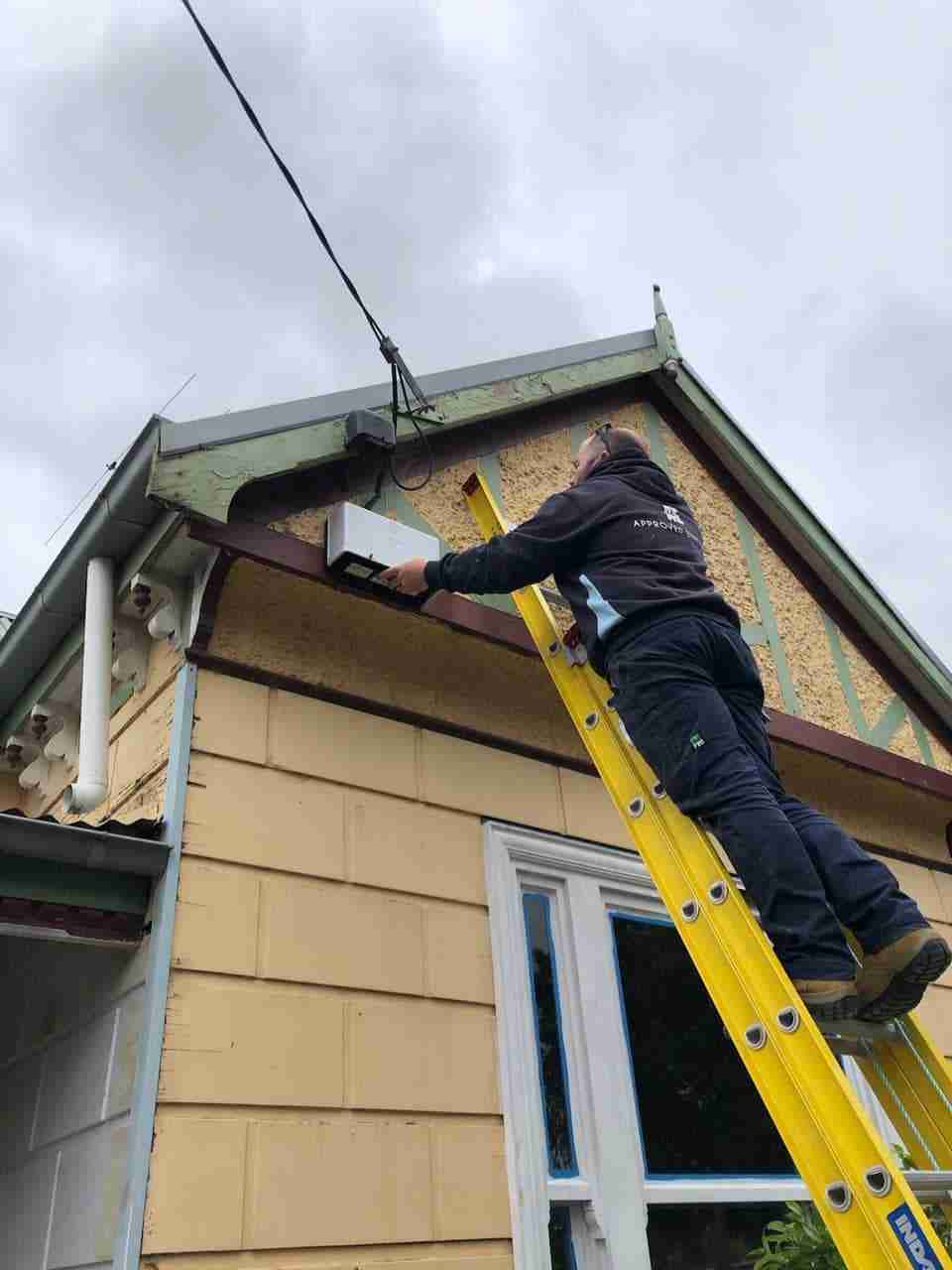 Approved Electrix emergency electrician Melbourne on a ladder fixing an outdoor light fixture on the exterior of a residential house.