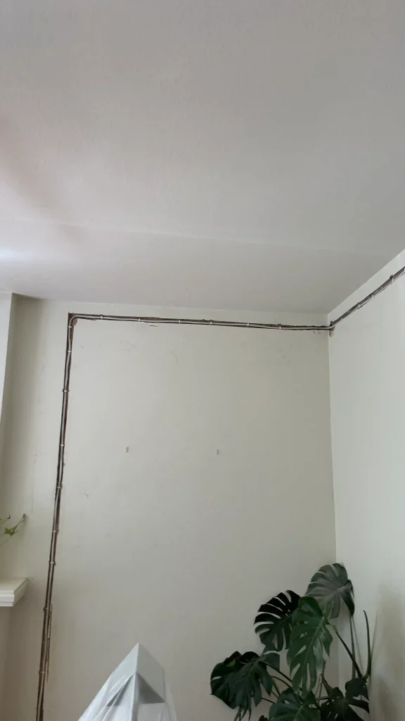 Corner of a room with ceiling damage showing exposed beams and cracks.