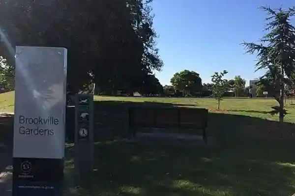 Brookville Gardens sign and bench in a green park setting, Toorak."