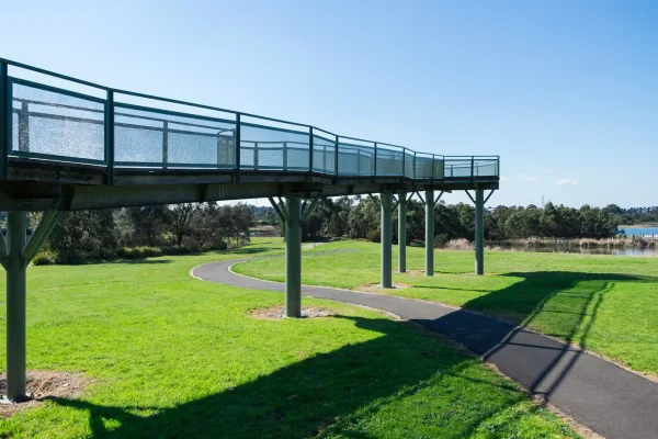 Elevated metal walkway over a lush park with a curving path and vibrant green grass in Moorabbin