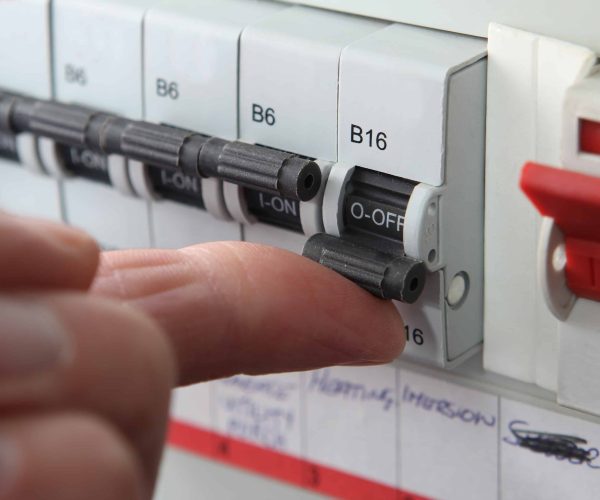An electrician wearing gloves is meticulously wiring a wall socket, with a multimeter in hand to ensure a safe and accurate installation amidst an array of tools and equipment.